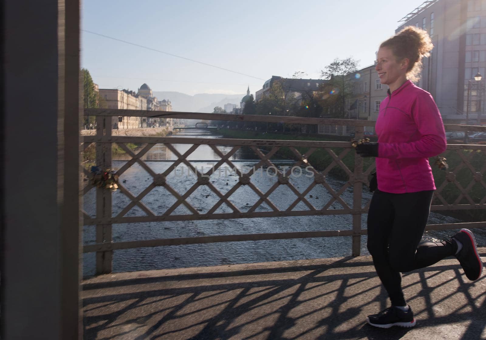 sporty woman running on sidewalk at early morning jogging with city  sunrise scene in background