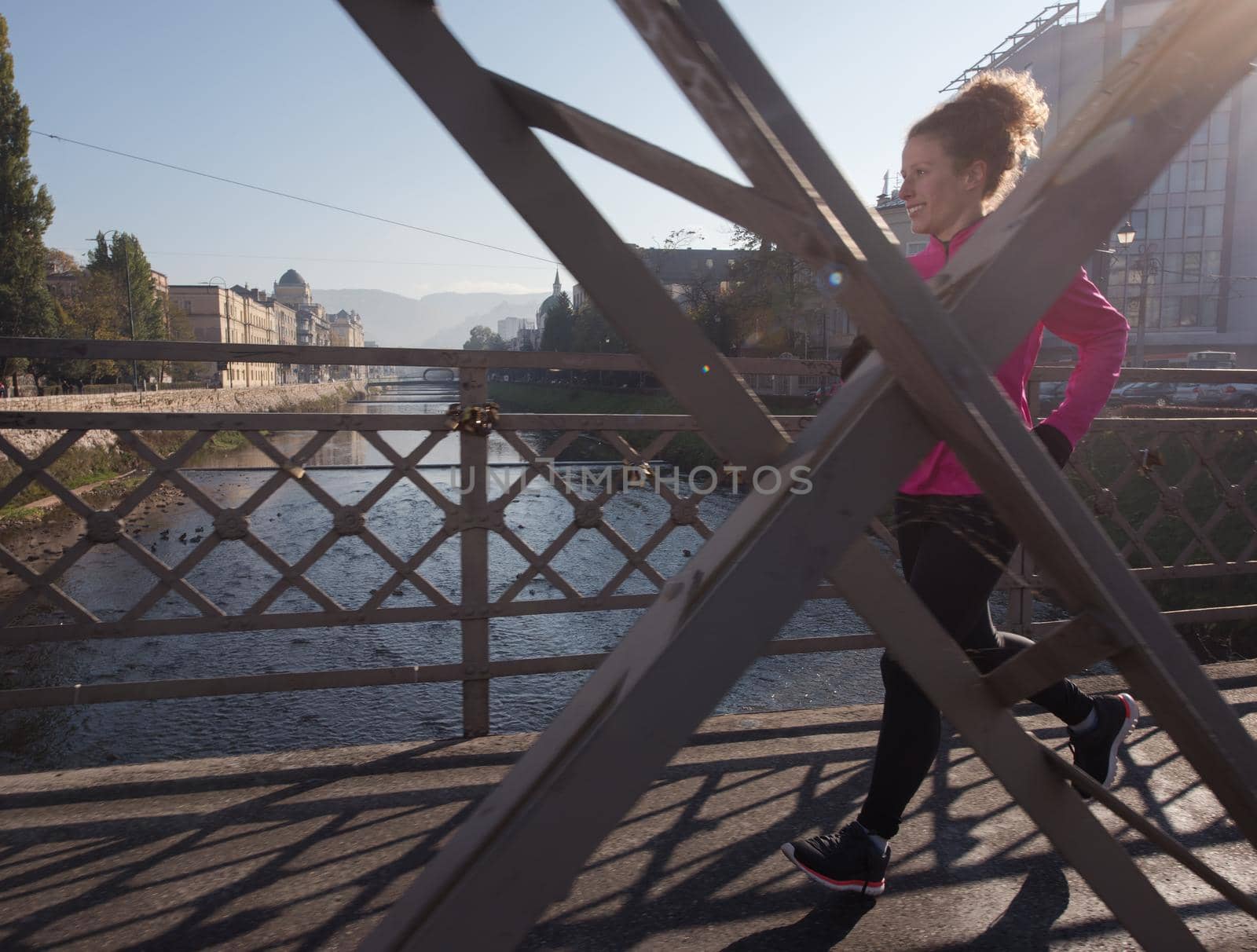 sporty woman running on sidewalk at early morning jogging with city  sunrise scene in background