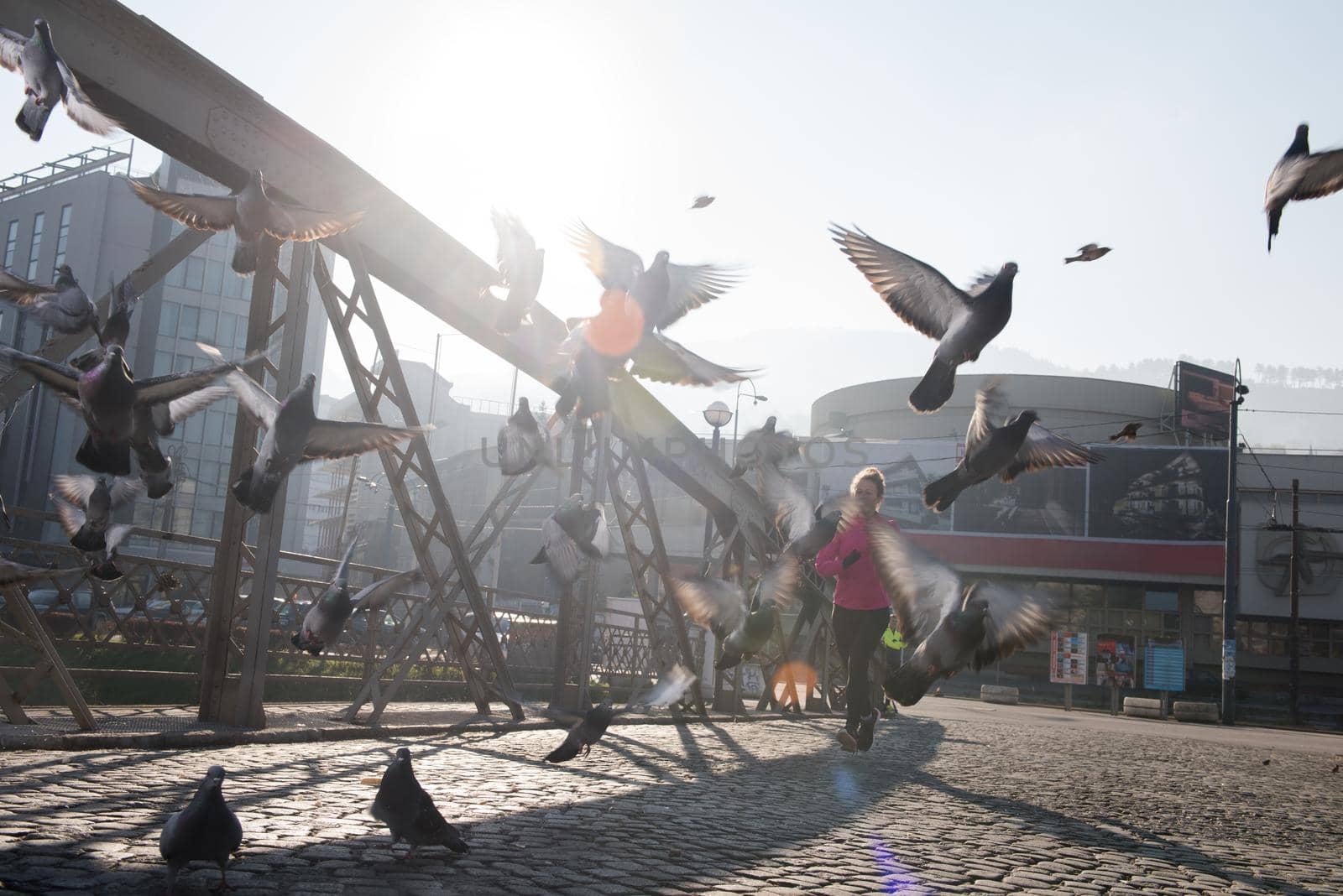 sporty woman running on sidewalk at early morning jogging with city  sunrise scene in background