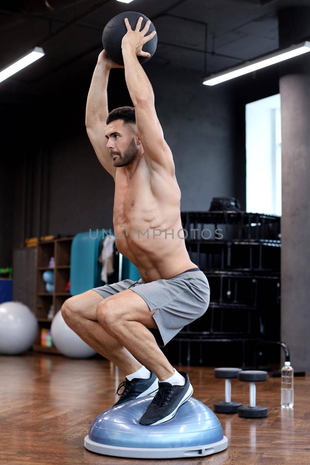 Fit and muscular man exercising with medicine ball on gymnastic hemisphere bosu ball in gym