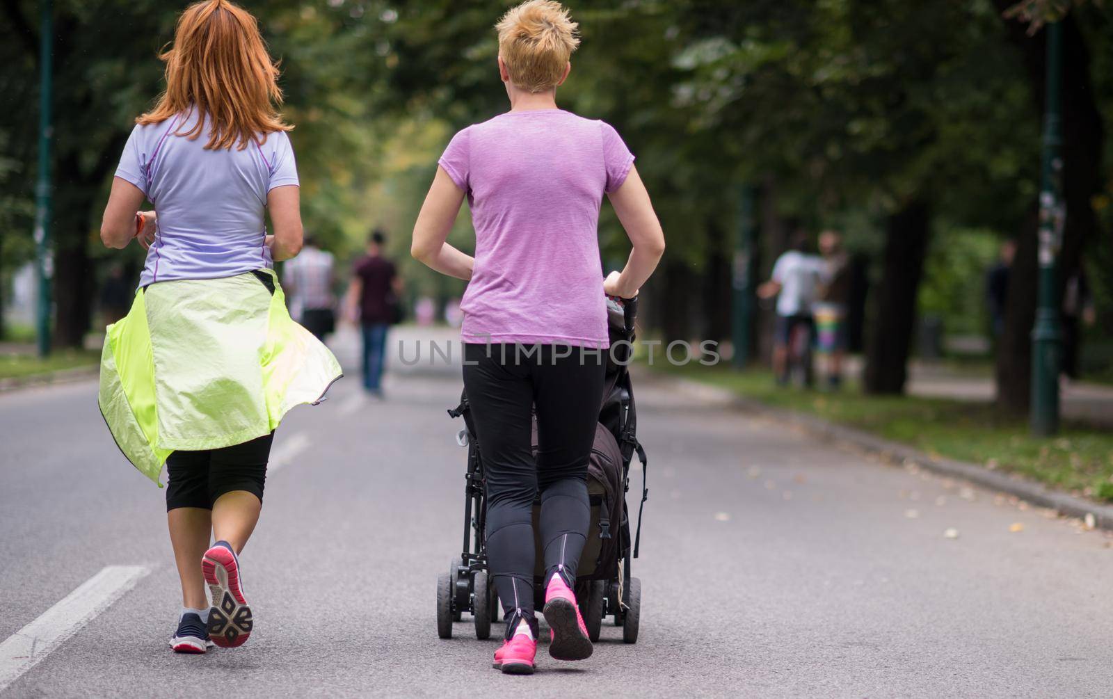 two young healthy women jogging together while pushing a baby stroller at city park