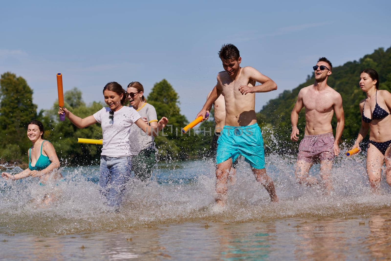 Summer joy group of happy friends having fun while running and splashing on river