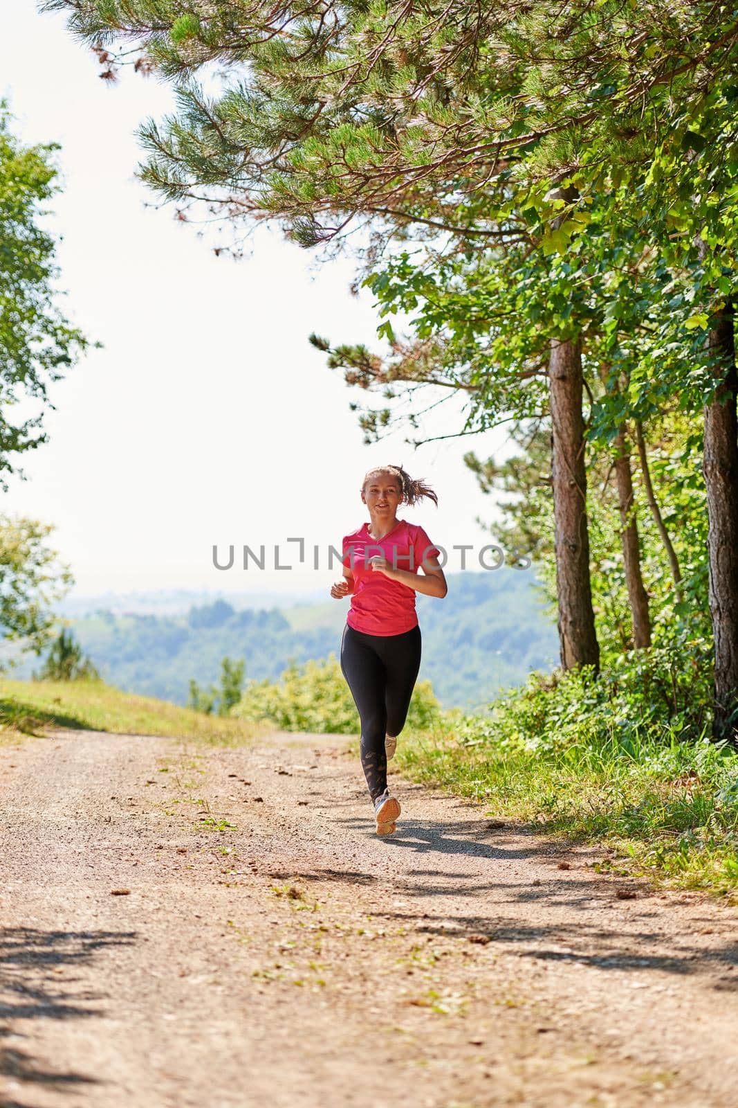 woman enjoying in a healthy lifestyle while jogging on a country road through the beautiful sunny forest, exercise and fitness concept