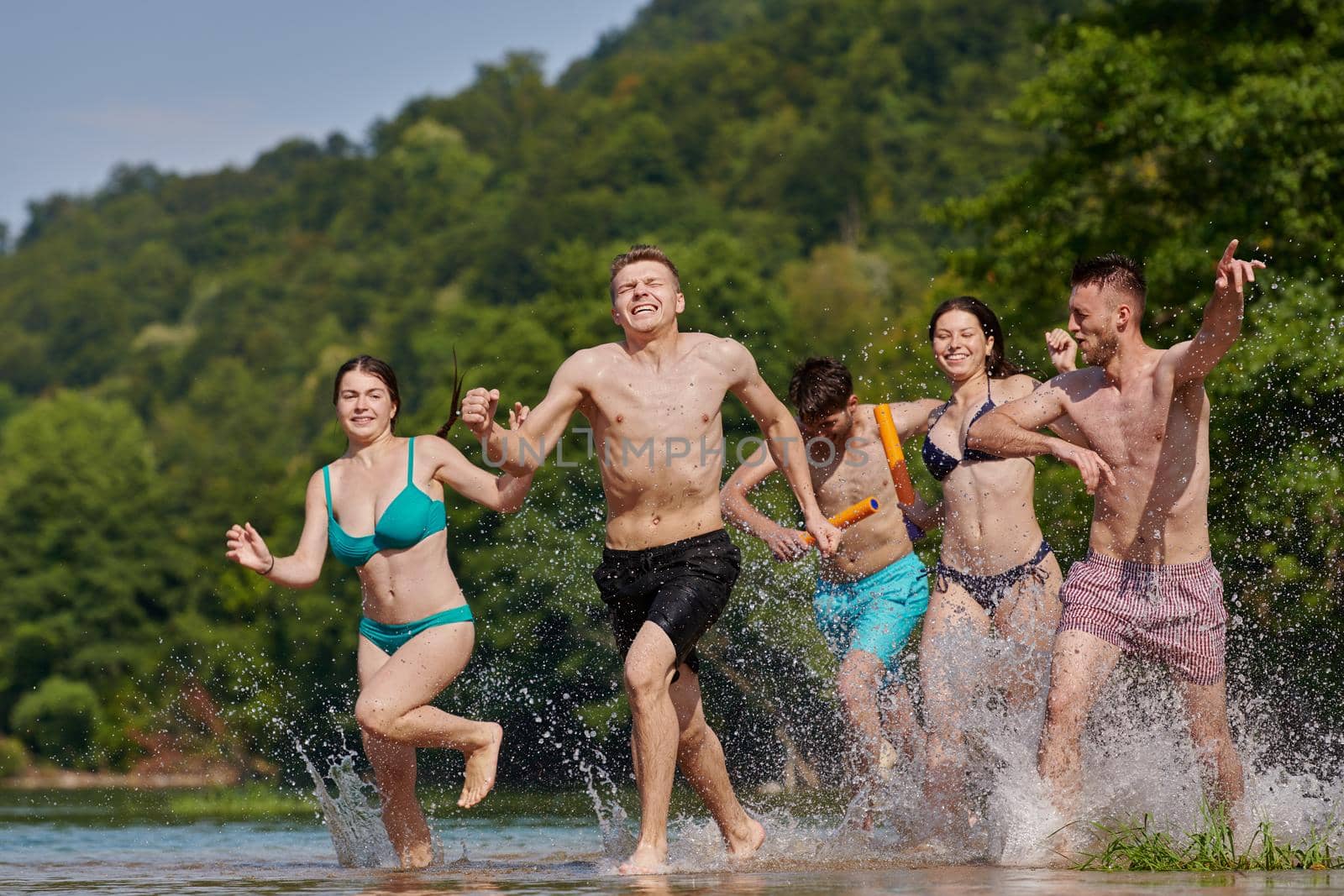 Summer joy group of happy friends having fun while running and splashing on river