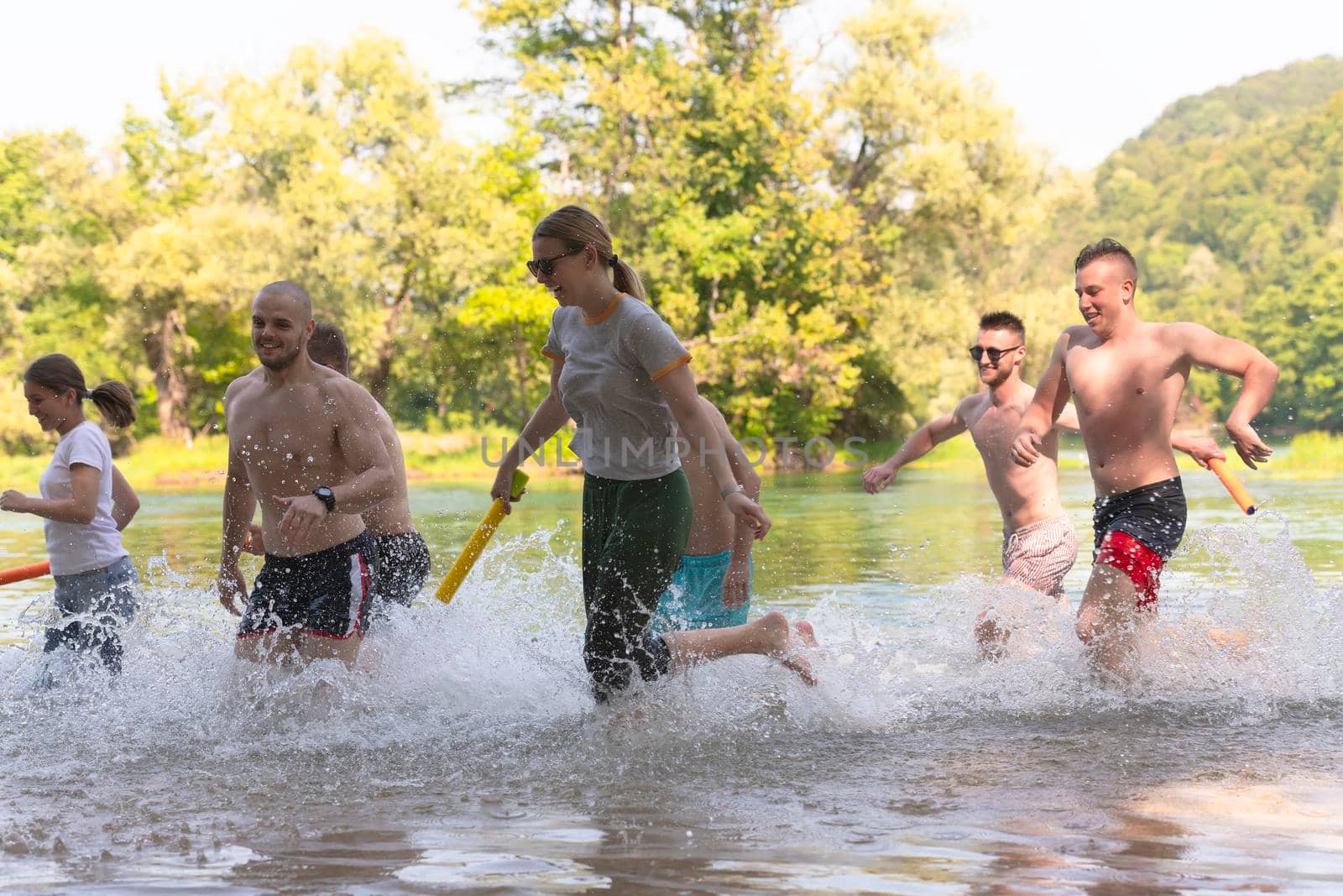 Summer joy group of happy friends having fun while running and splashing on river