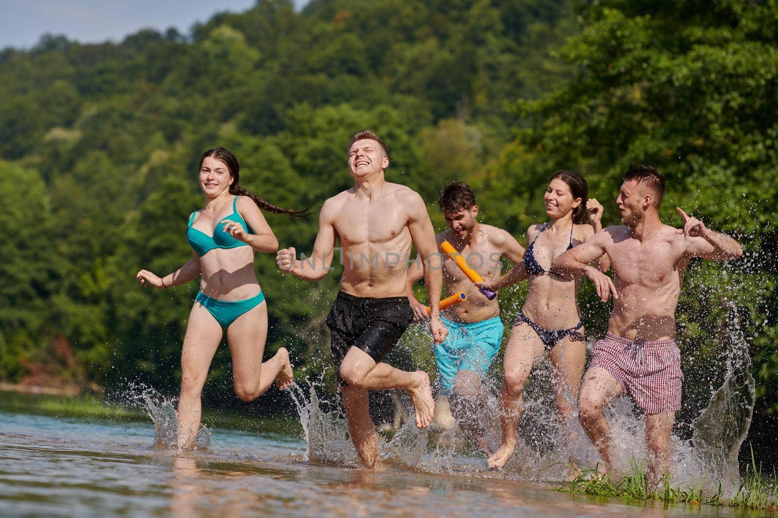 Summer joy group of happy friends having fun while running and splashing on river