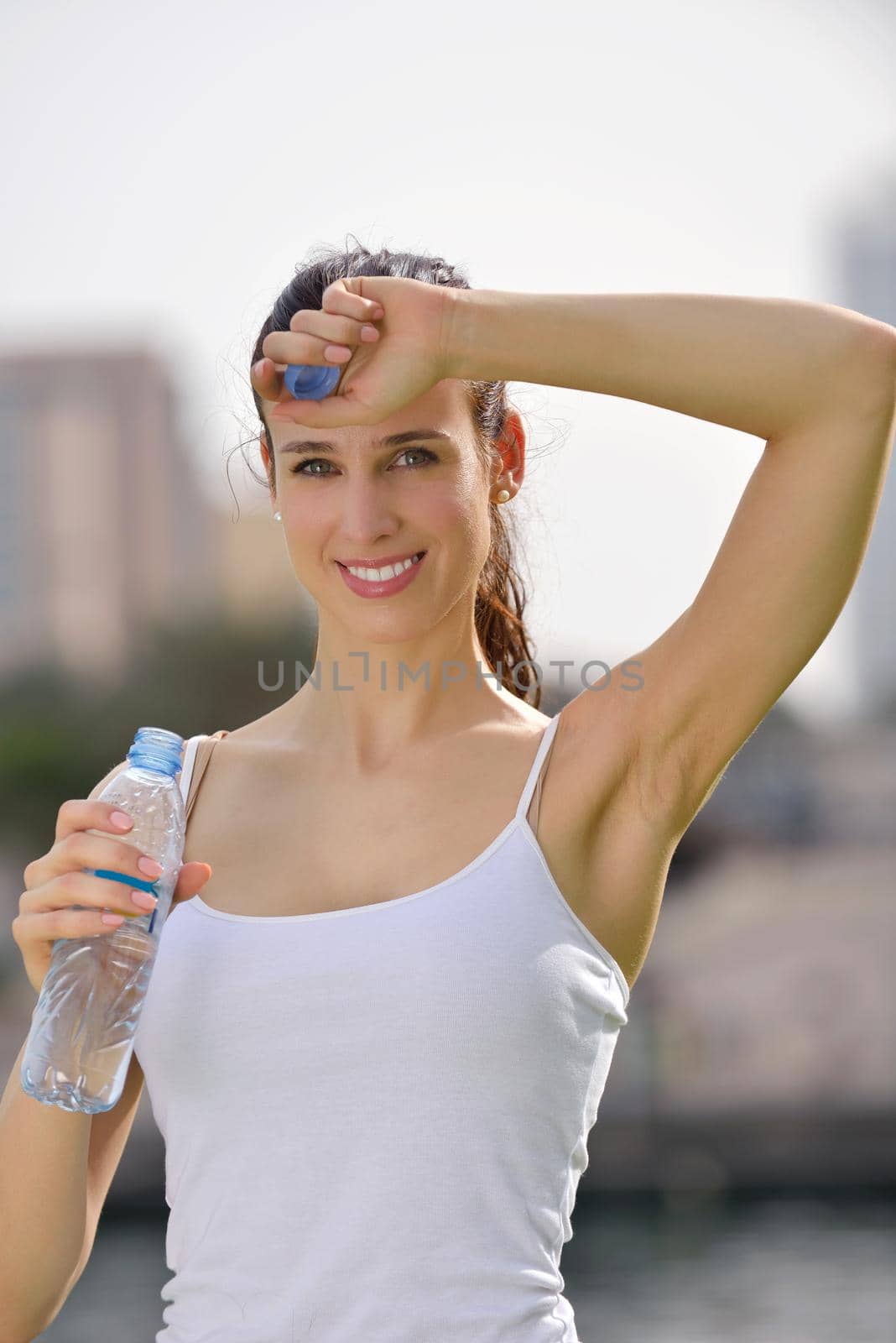 Young beautiful woman drinking water after fitness exercise and jogging outdoors