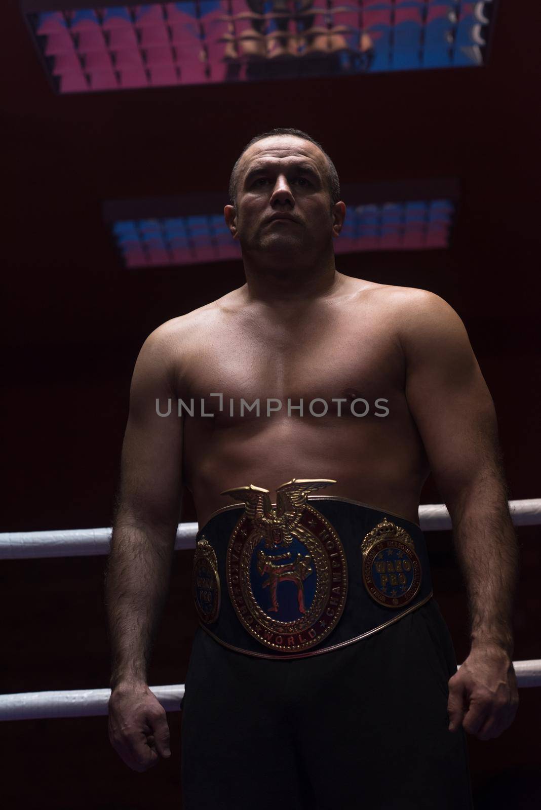 portrait of muscular professional kick boxer with his championship belt in the training ring