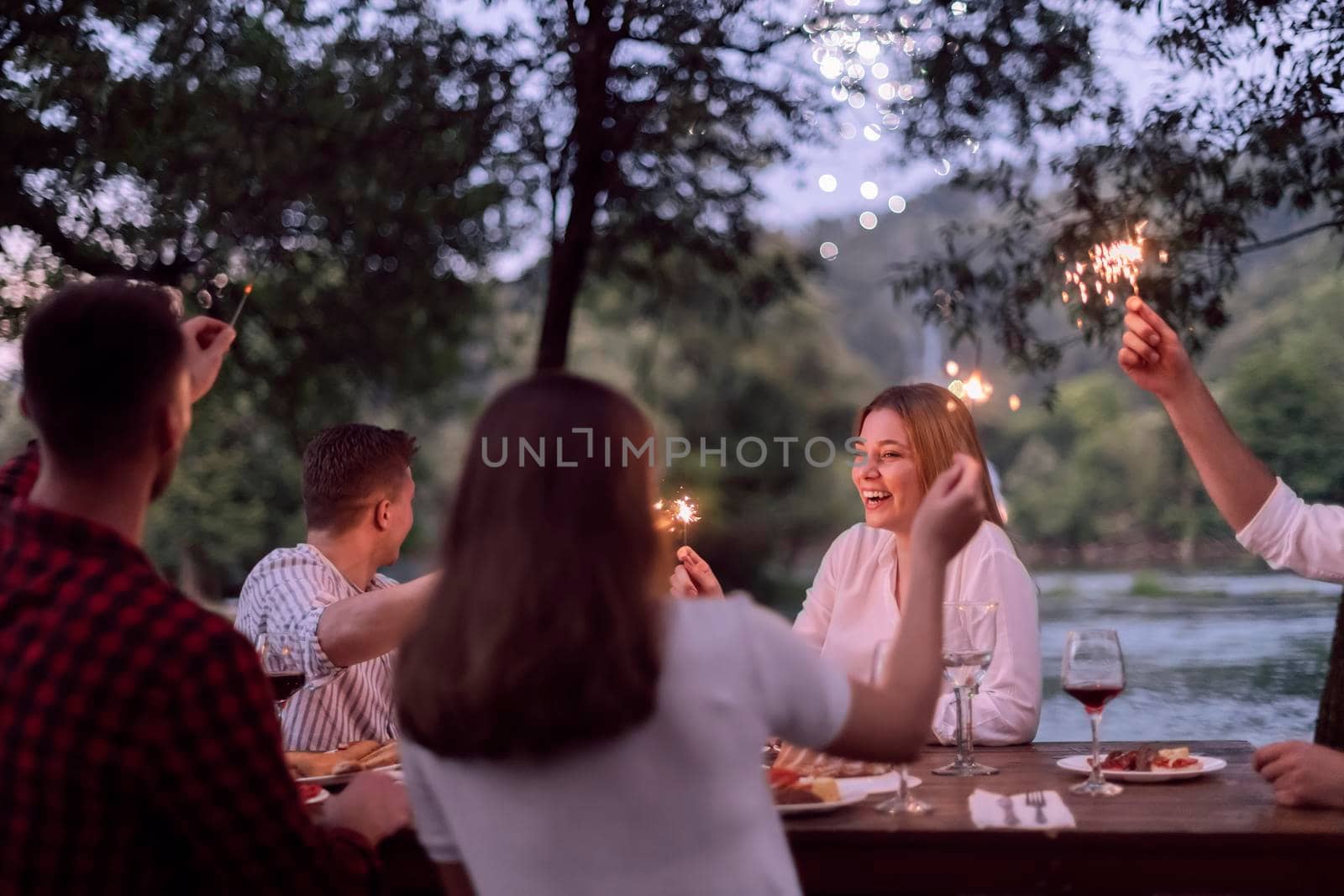 group of happy friends having picnic french dinner party outdoor during summer holiday vacation near the river at beautiful nature