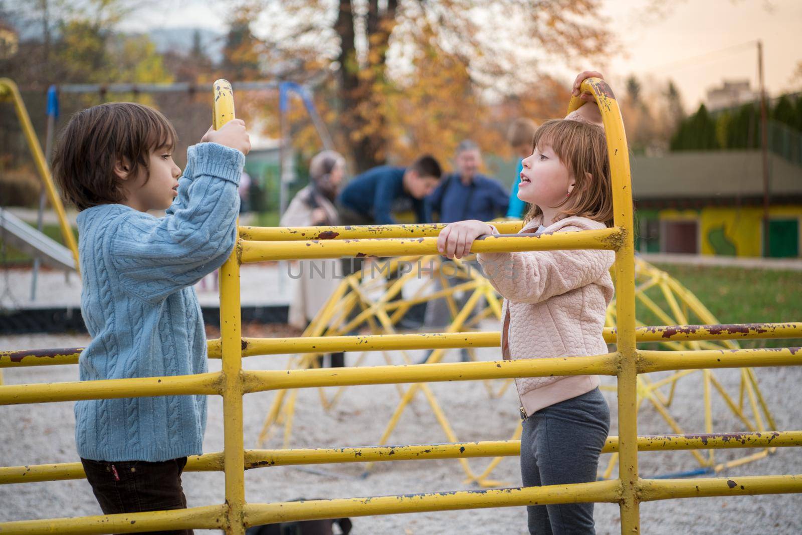 cutte little girl and boy in childrens park having fun and joy while playing in playground on autumn cloudy day