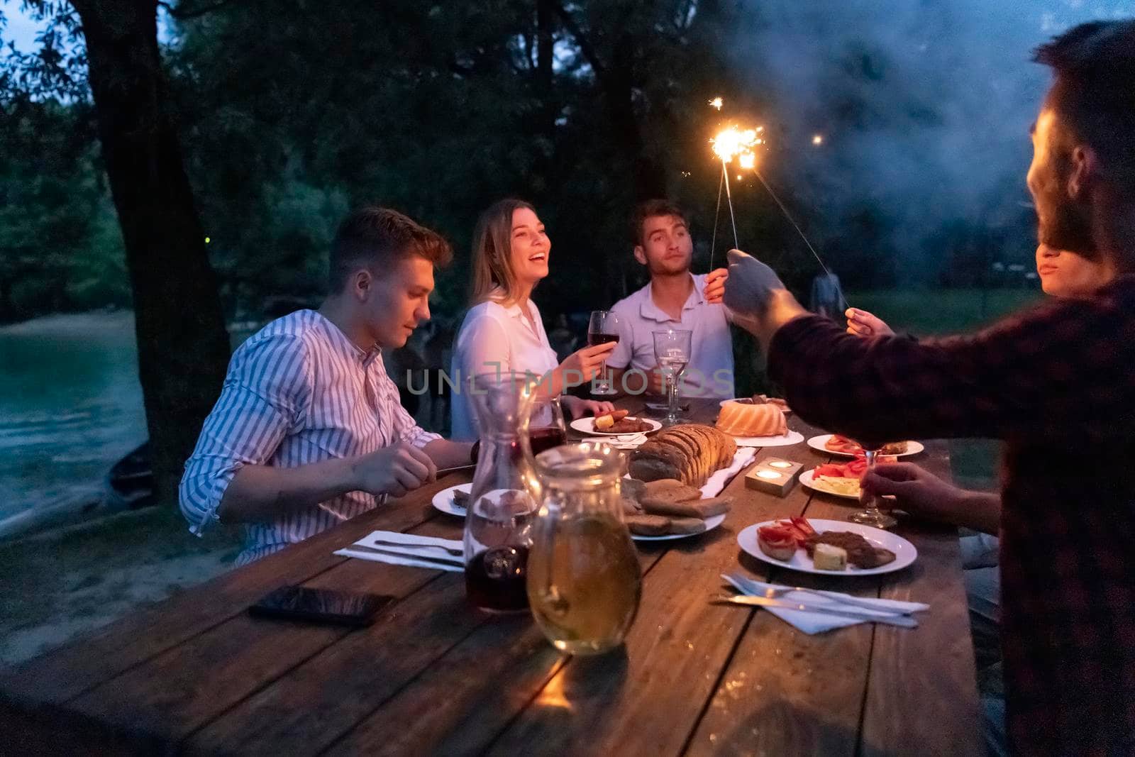 group of happy friends having picnic french dinner party outdoor during summer holiday vacation near the river at beautiful nature