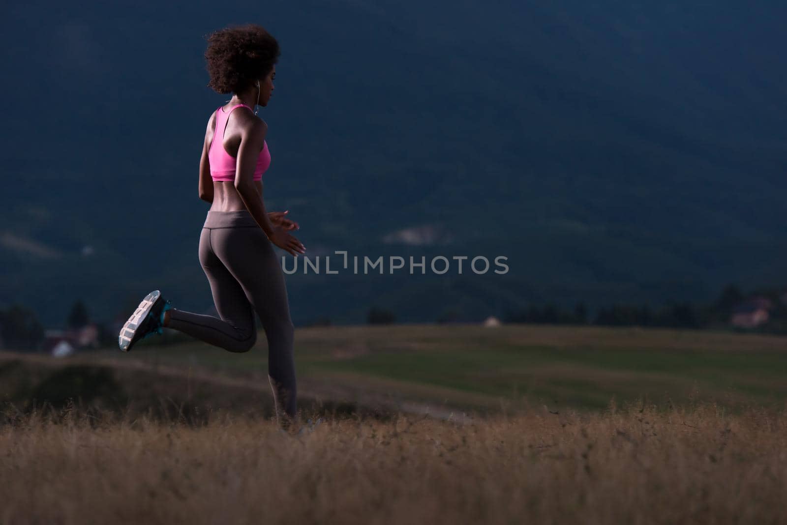 young African american woman runner with headphones jogging outdoors in nature beautiful summer night - Fitness, people and healthy lifestyle