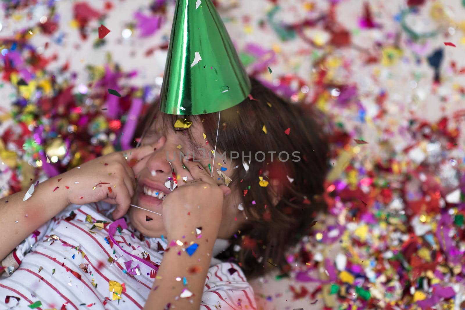 Happy kid celebrating party with blowing confetti while lying on the floor