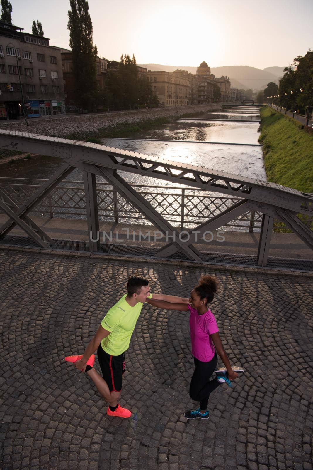 Young multiethnic jogging couple warming up and stretching before morning running in the city