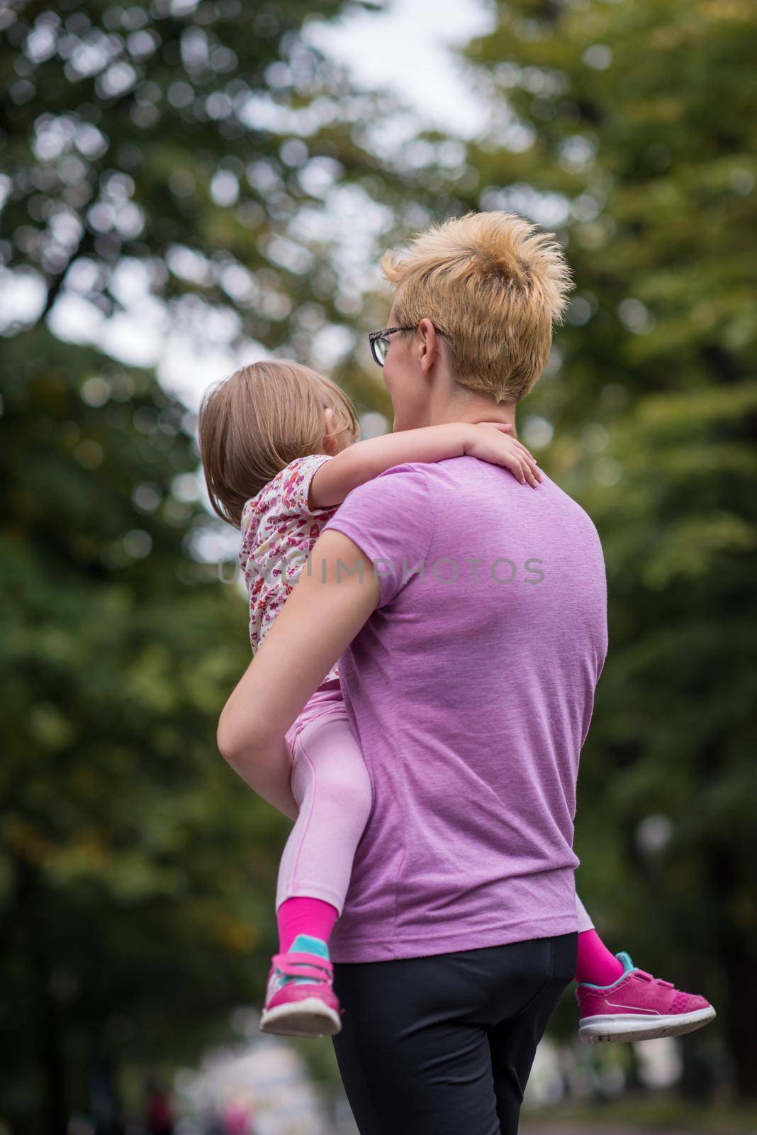 young sporty mother carries little daughter in arms while jogging in a city park,outdoor sports and fitness