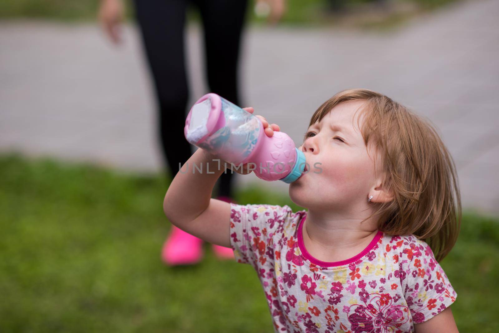 happy little girl drinking fresh water from a bottle while running at city park