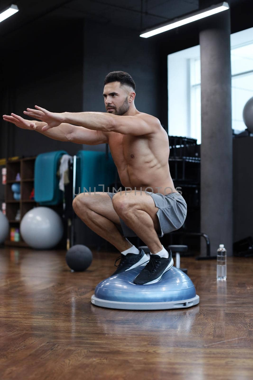 Fit athlete performing exercise on gymnastic hemisphere bosu ball in gym