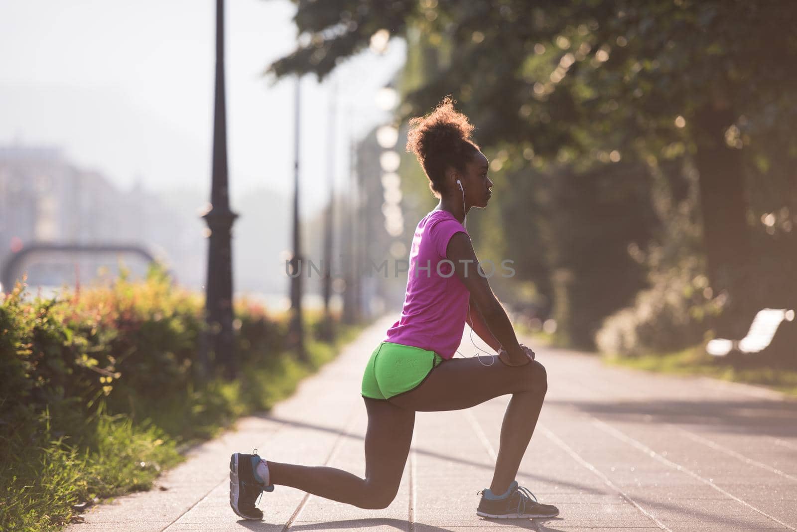 young beautiful African American woman doing warming up and stretching before the morning run with the sunrise in the background