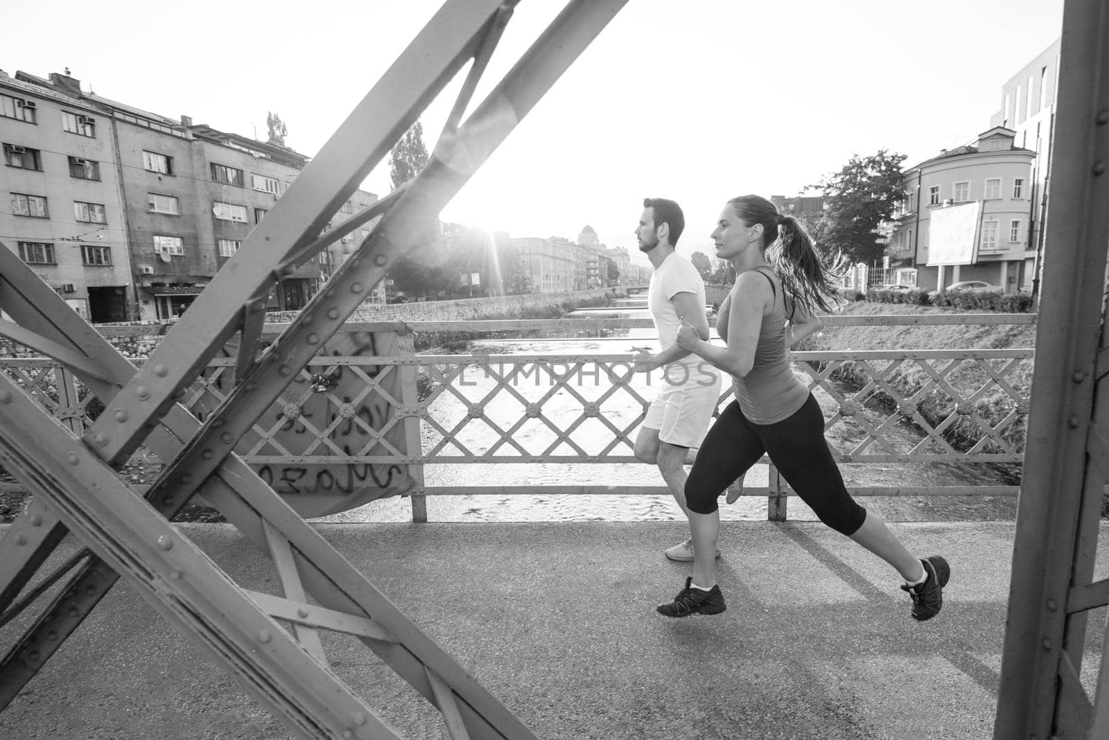 urban sports, healthy young couple jogging across the bridge in the city at sunny morning