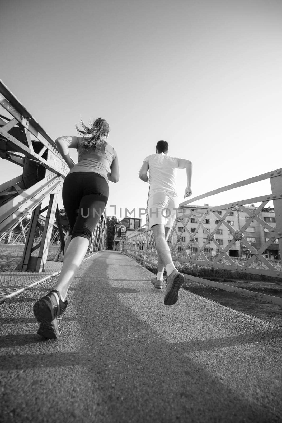young couple jogging across the bridge in the city by dotshock