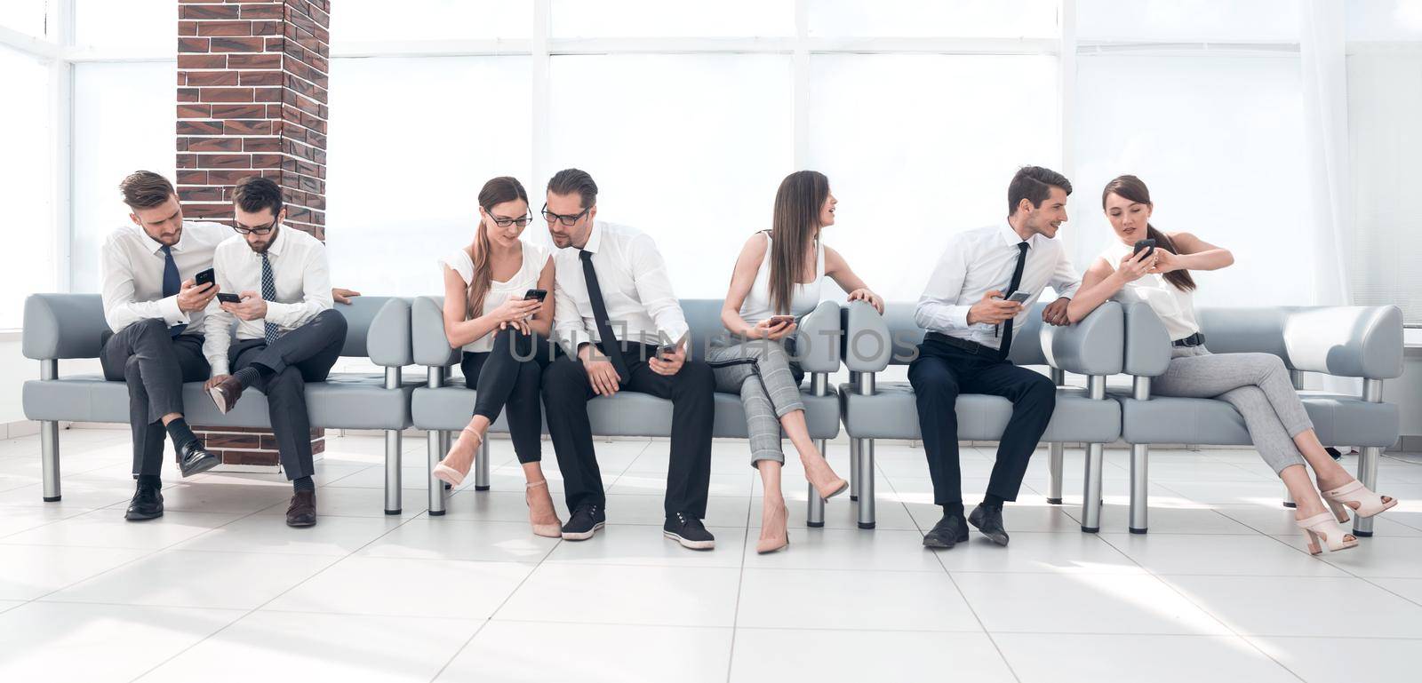 group of employees use smartphones while sitting in the office lobby by asdf