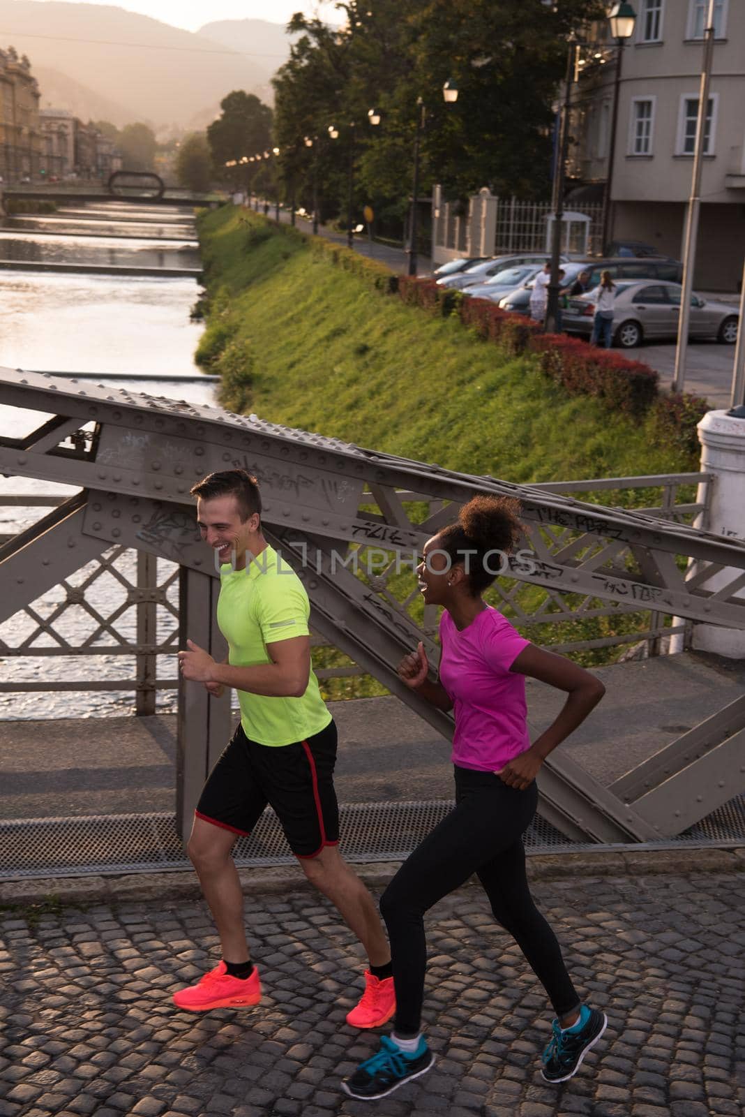 healthy young multiethnic couple jogging in the city at early morning with sunrise in background