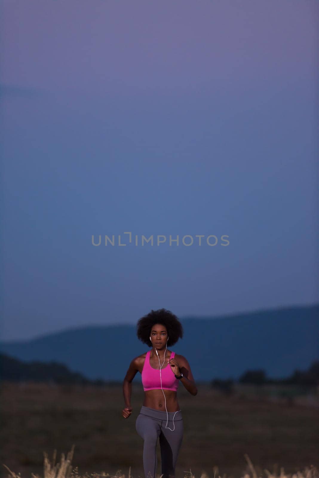 young African american woman runner with headphones jogging outdoors in nature beautiful summer night - Fitness, people and healthy lifestyle