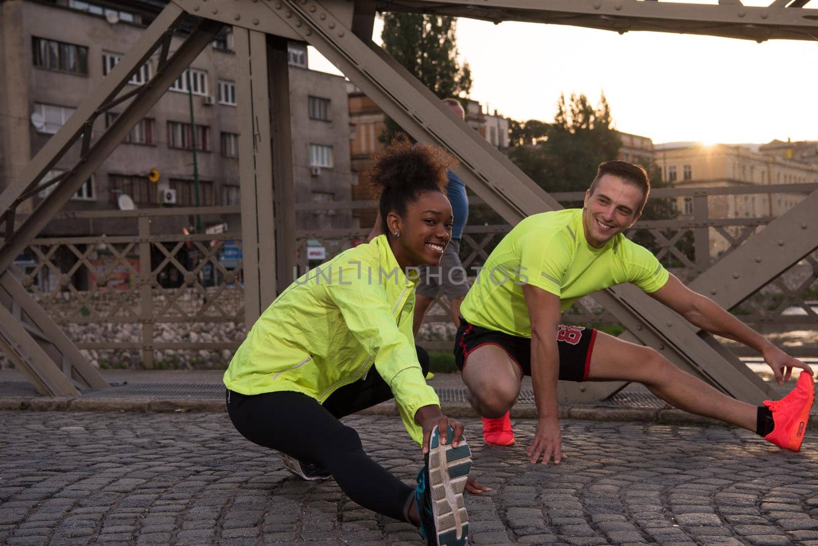 Young multiethnic jogging couple warming up and stretching before morning running in the city