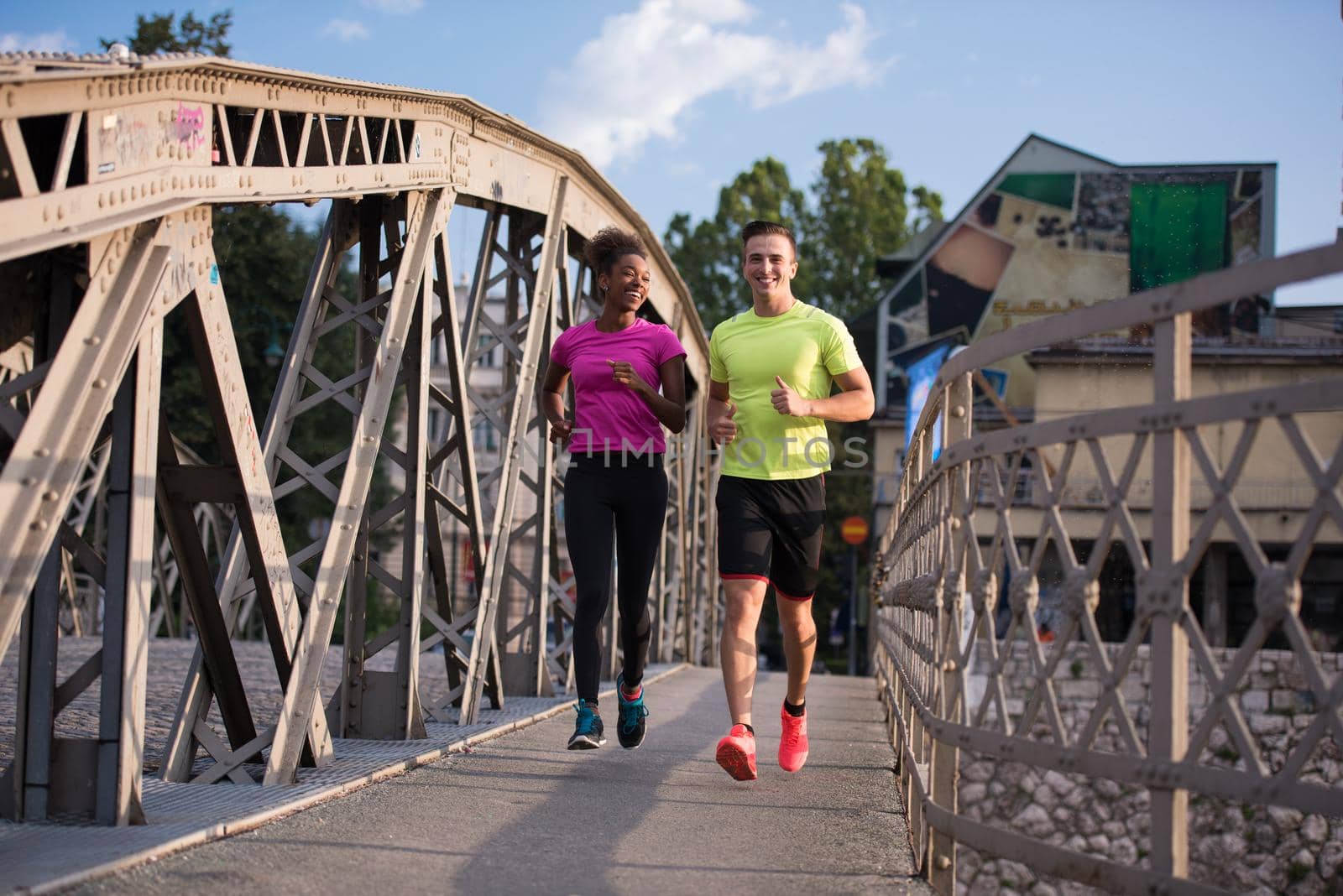 healthy young multiethnic couple jogging across the bridge in the city at early morning with sunrise in background