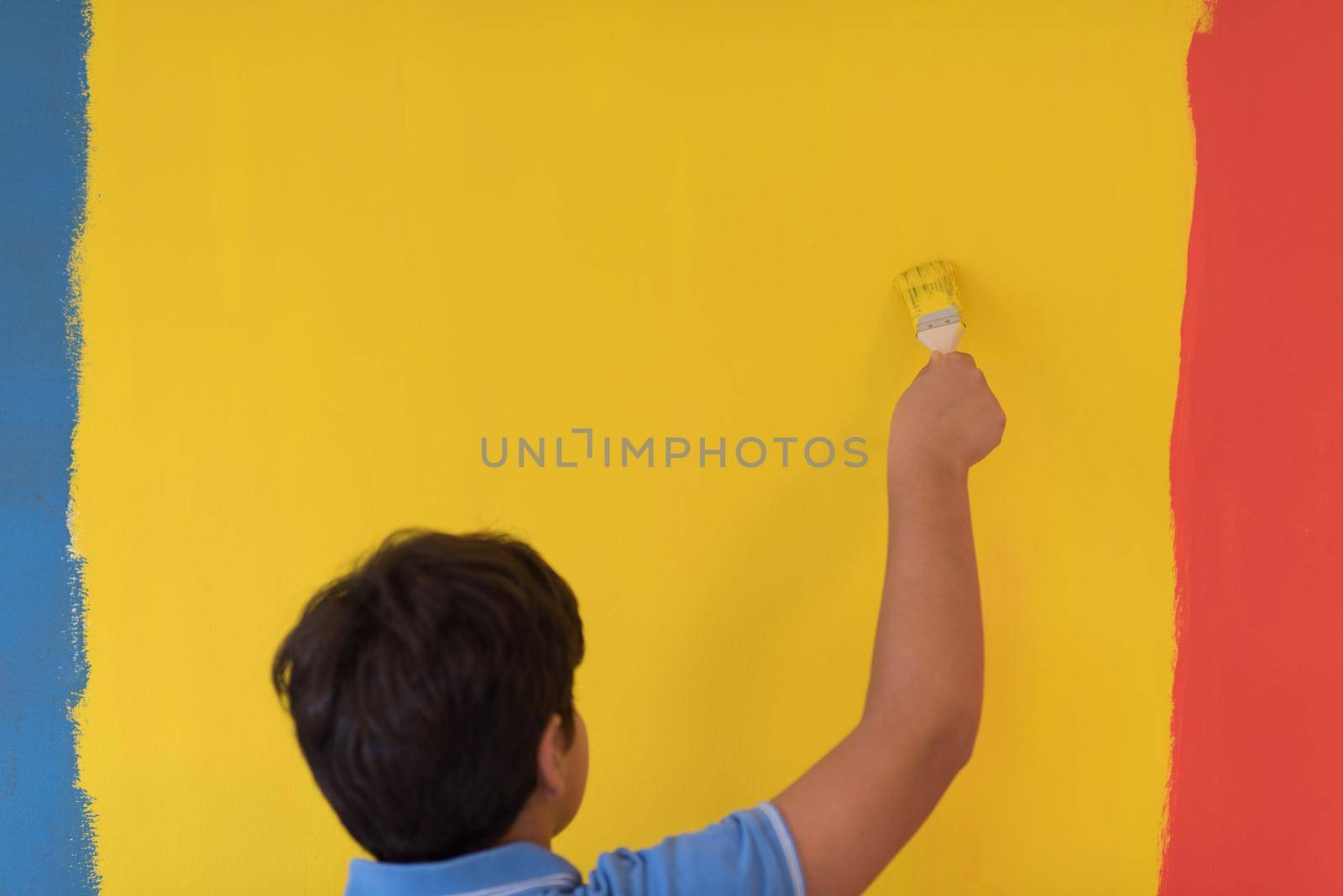 Portrait of a young boy painter with a brush in his hand in front of colored background