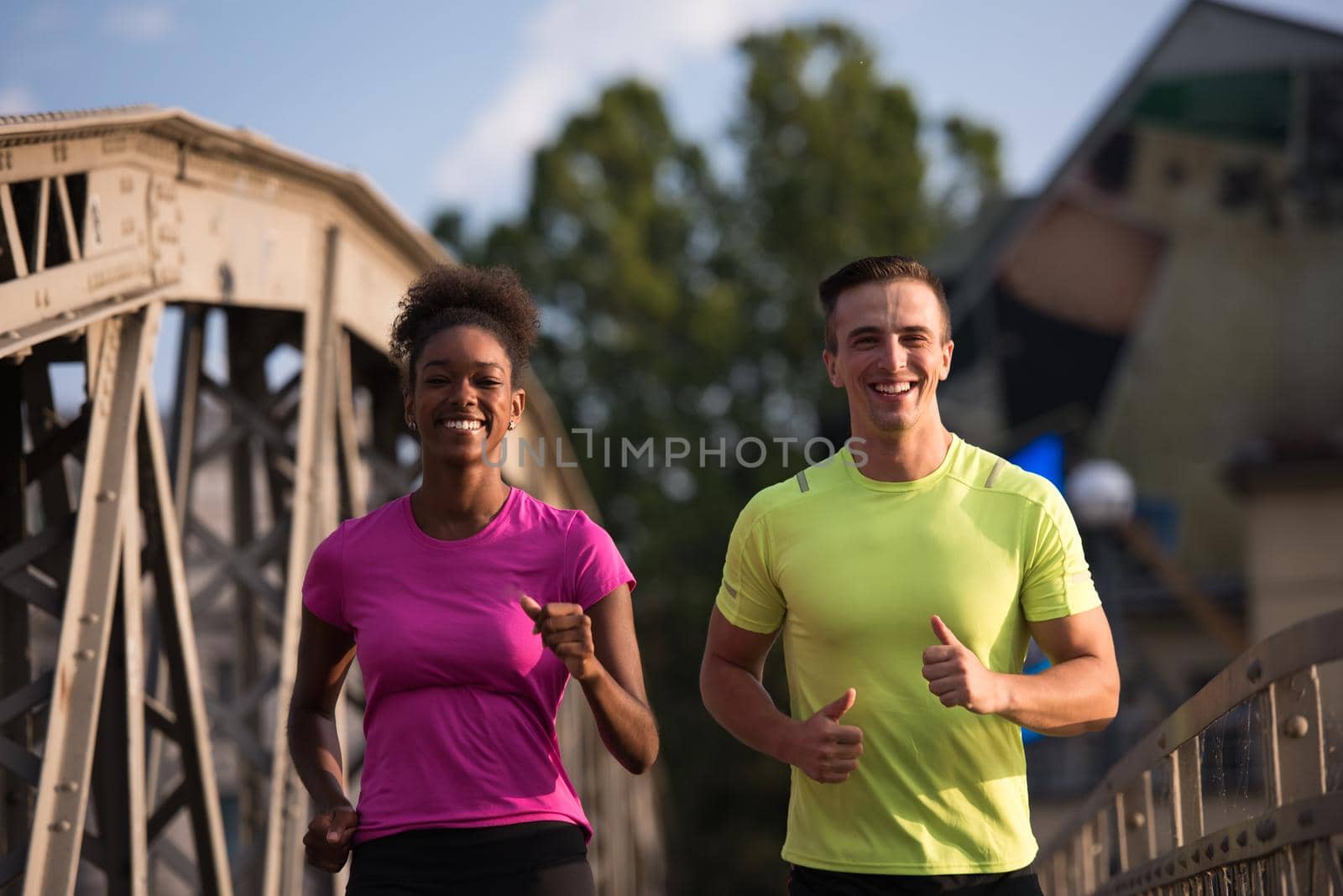 healthy young multiethnic couple jogging across the bridge in the city at early morning with sunrise in background