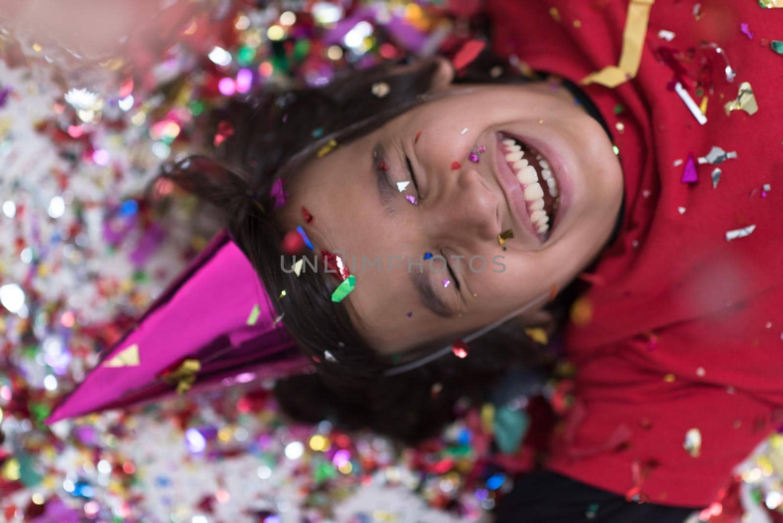 Happy kid celebrating party with blowing confetti while lying on the floor