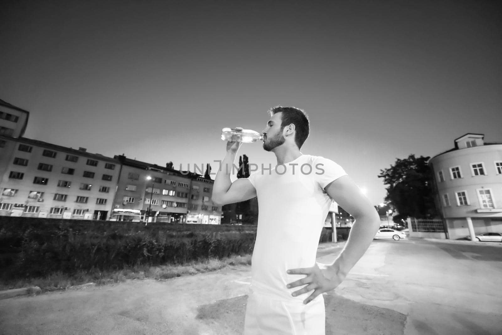 young athletic man drinking water after a night running session in the city