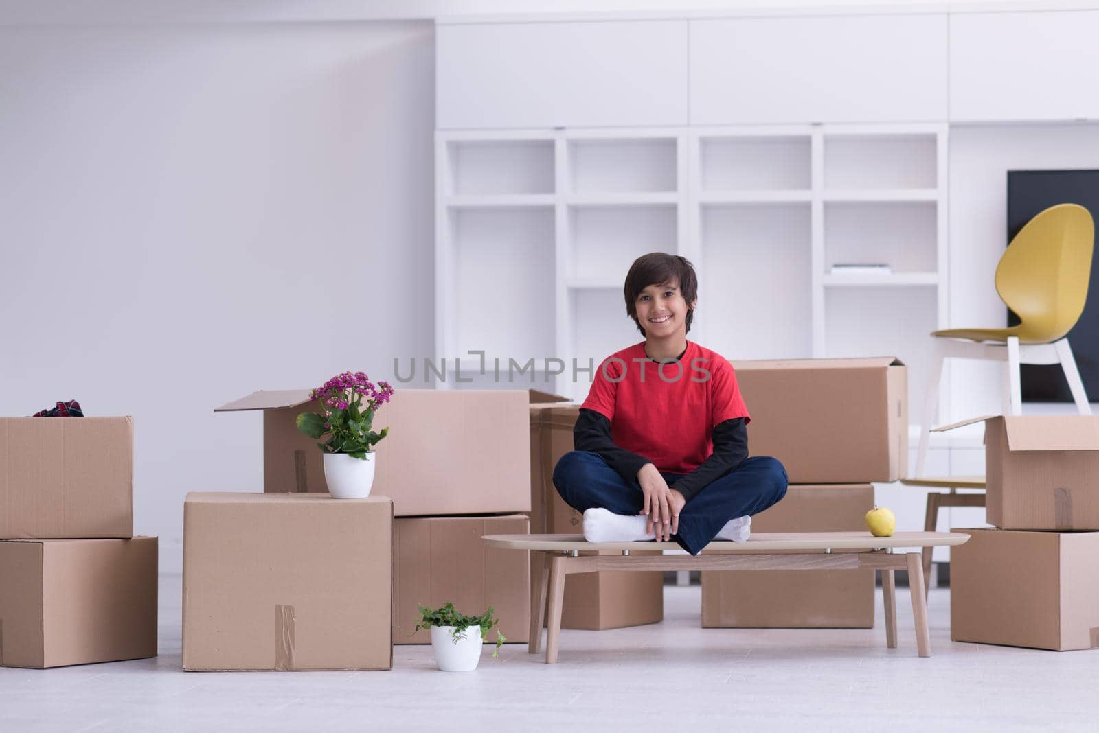happy little boy sitting on the table with cardboard boxes around him in a new modern home