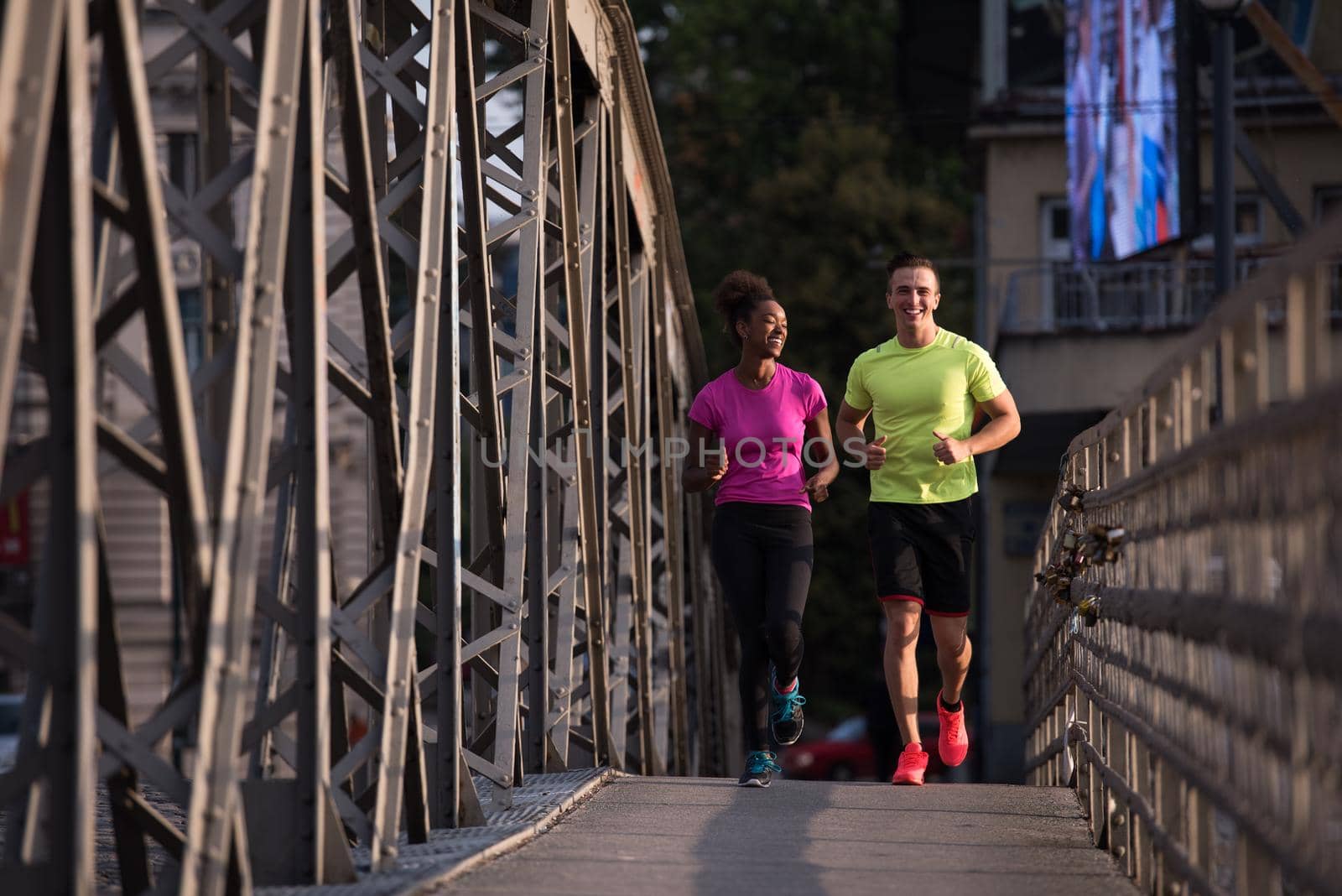 healthy young multiethnic couple jogging across the bridge in the city at early morning with sunrise in background