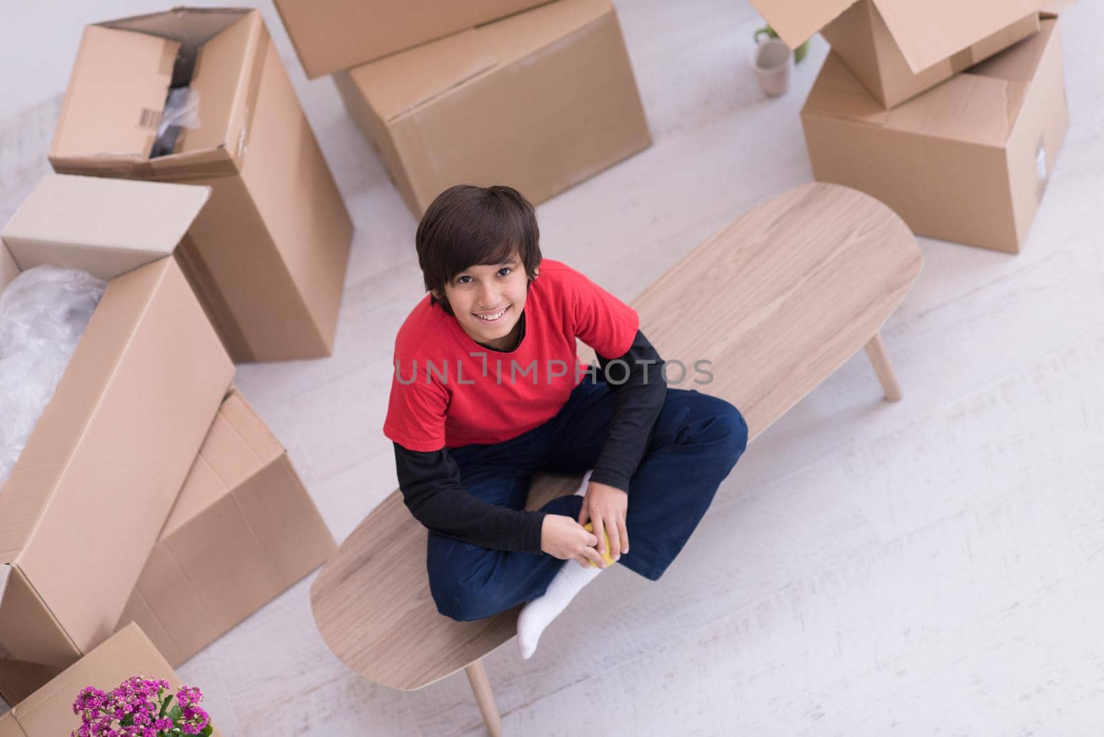 happy little boy sitting on the table with cardboard boxes around him in a new modern home,top view