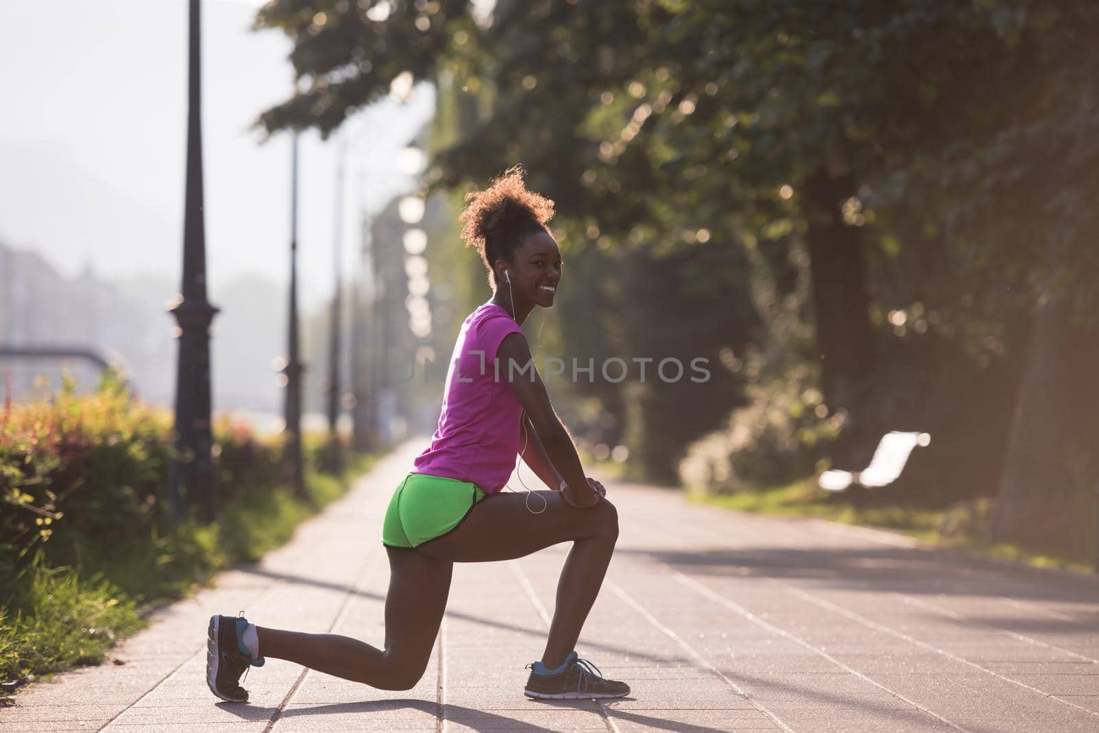 young beautiful African American woman doing warming up and stretching before the morning run with the sunrise in the background