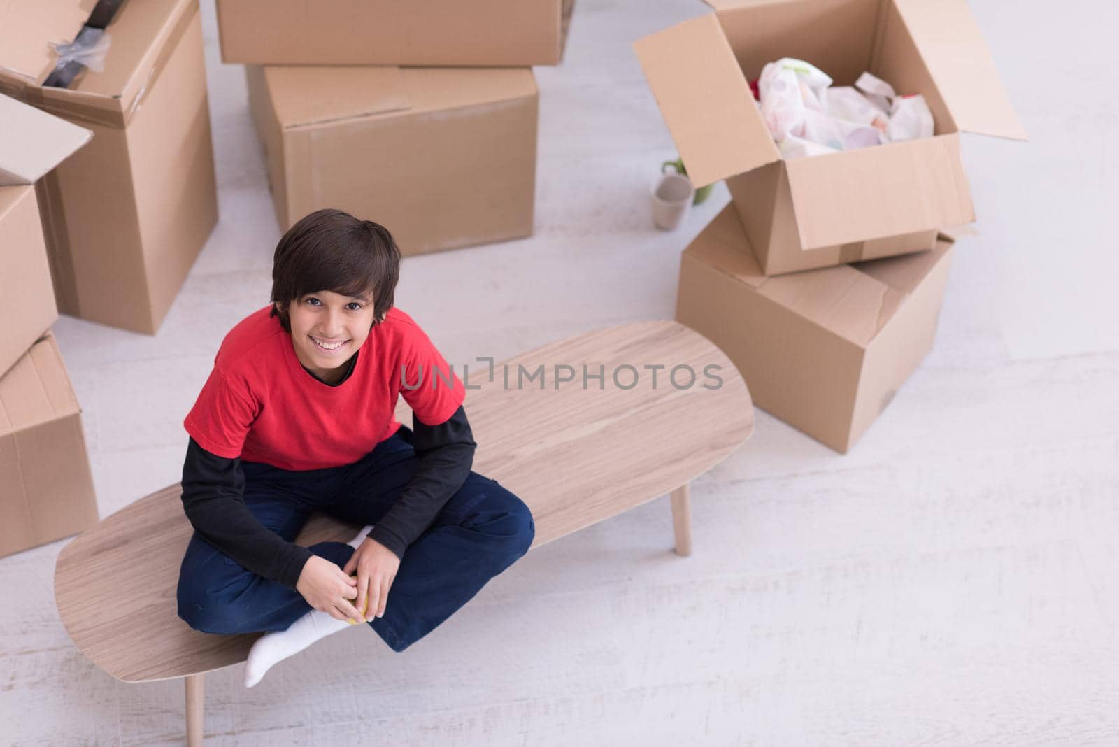 happy little boy sitting on the table with cardboard boxes around him in a new modern home,top view
