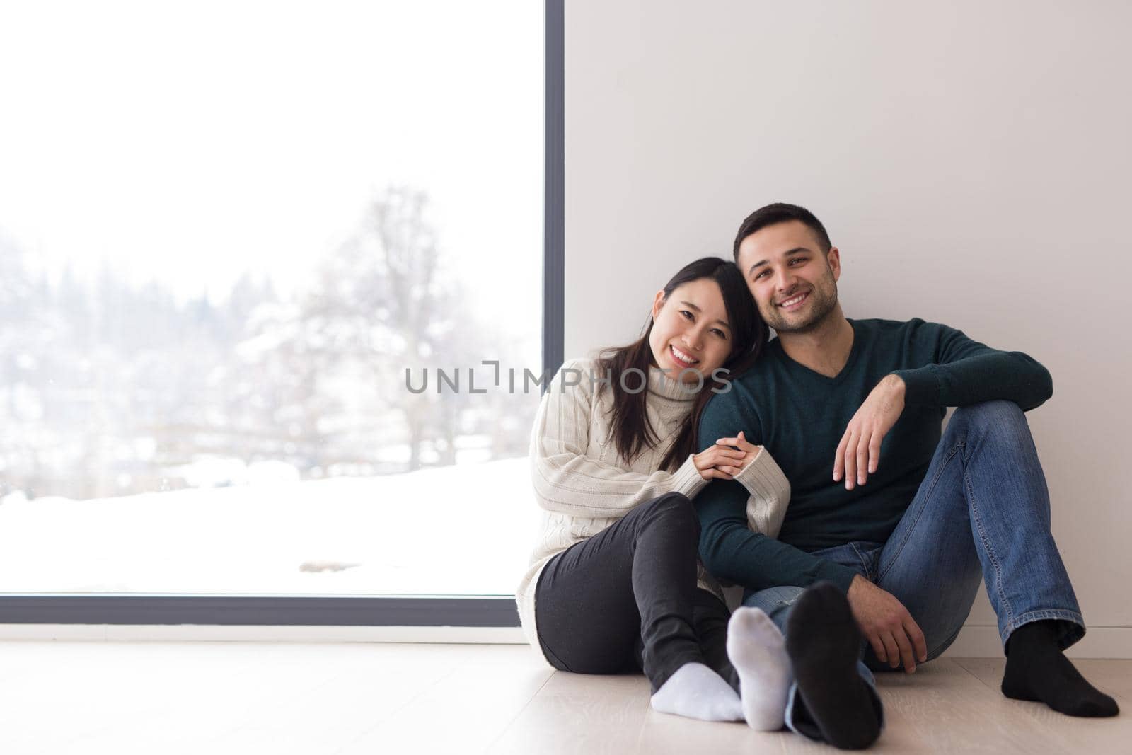 multiethnic couple sitting on the floor near window at home by dotshock