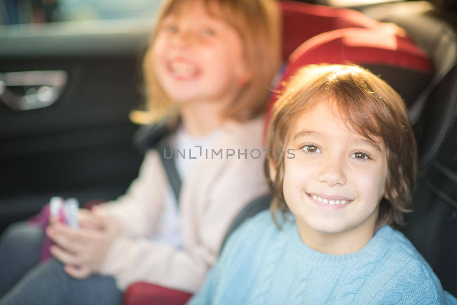 happy kids girl with her brother sitting together in modern car children seats locked with safety belts
