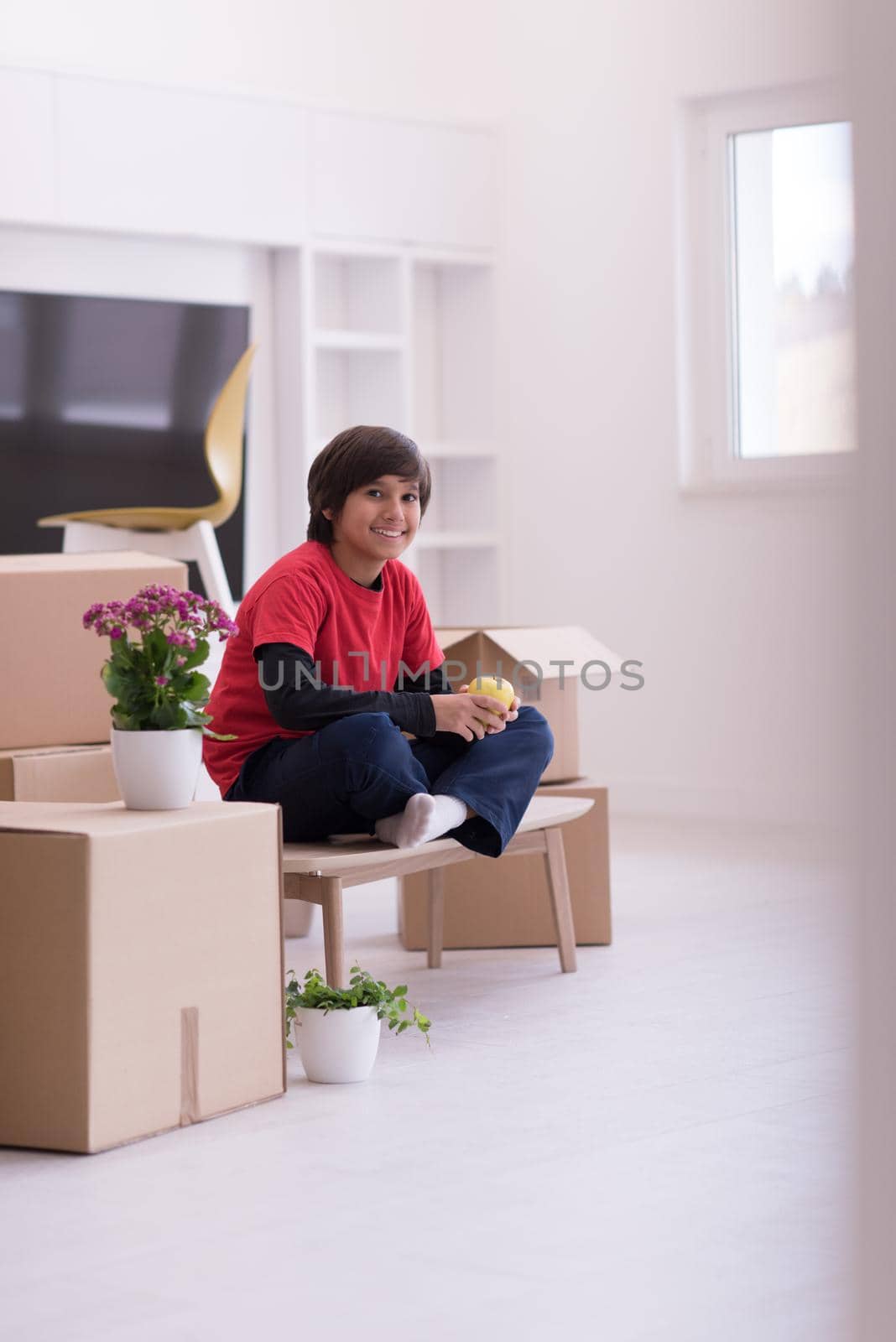 happy little boy sitting on the table with cardboard boxes around him in a new modern home