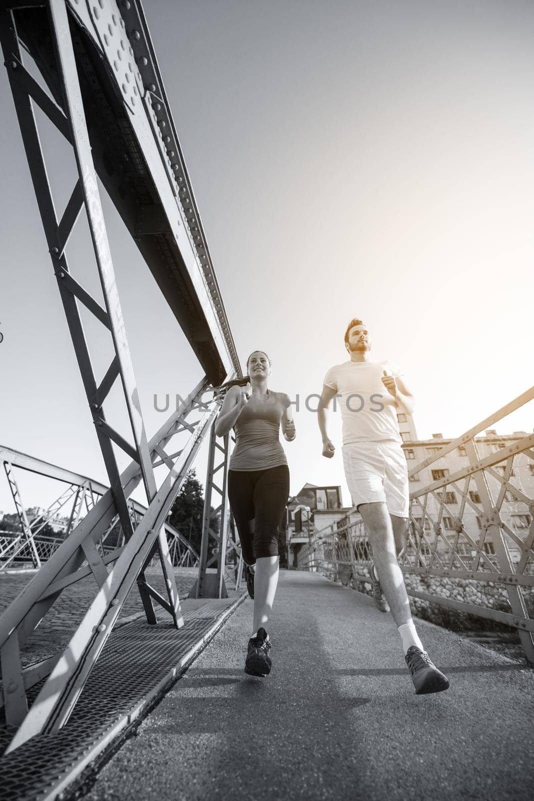 urban sports, healthy young couple jogging across the bridge in the city at sunny morning