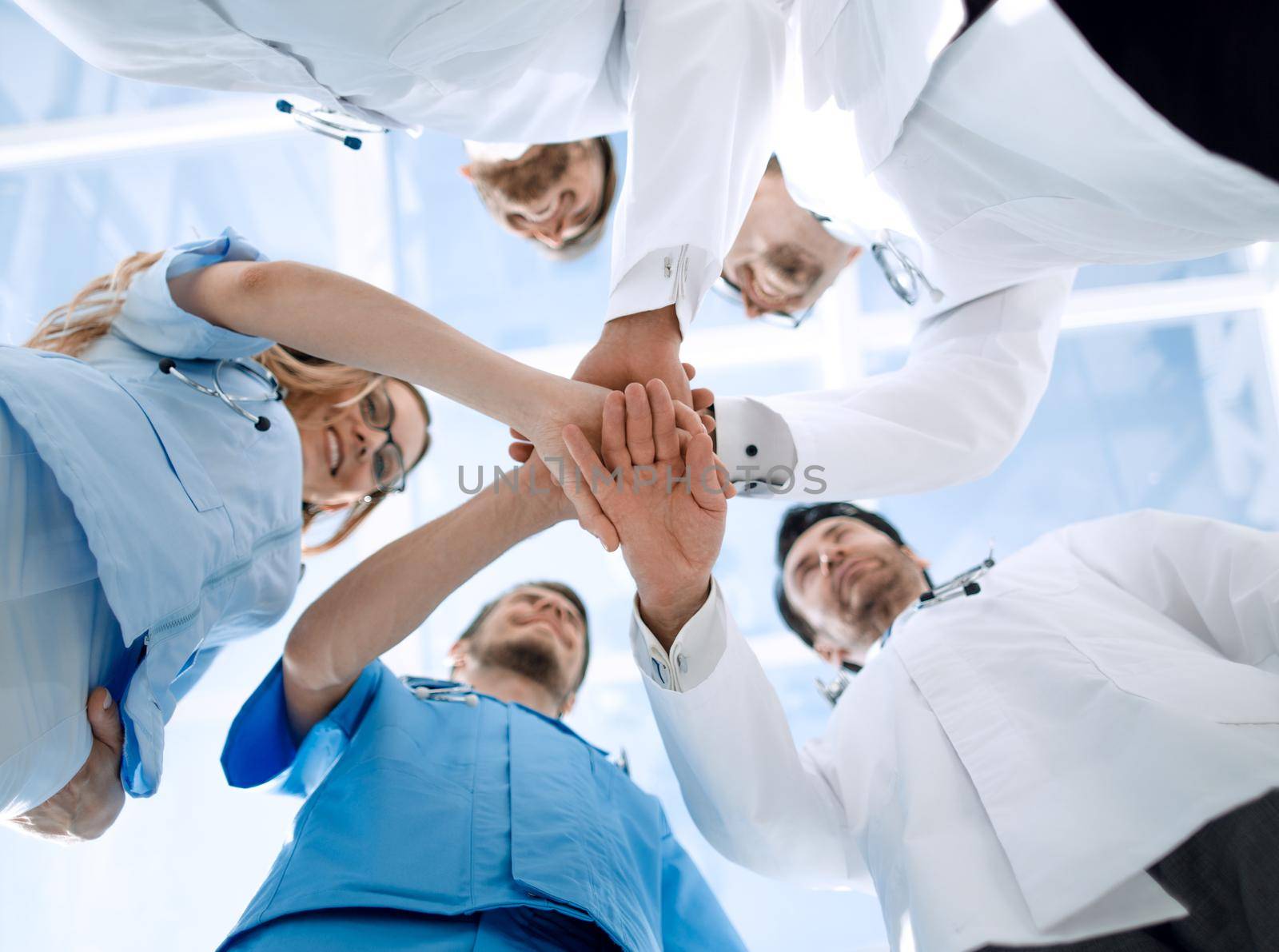 A group of doctors are holding each other's hands. They demonstrate close cooperation and friendship. They work in the hospital.
