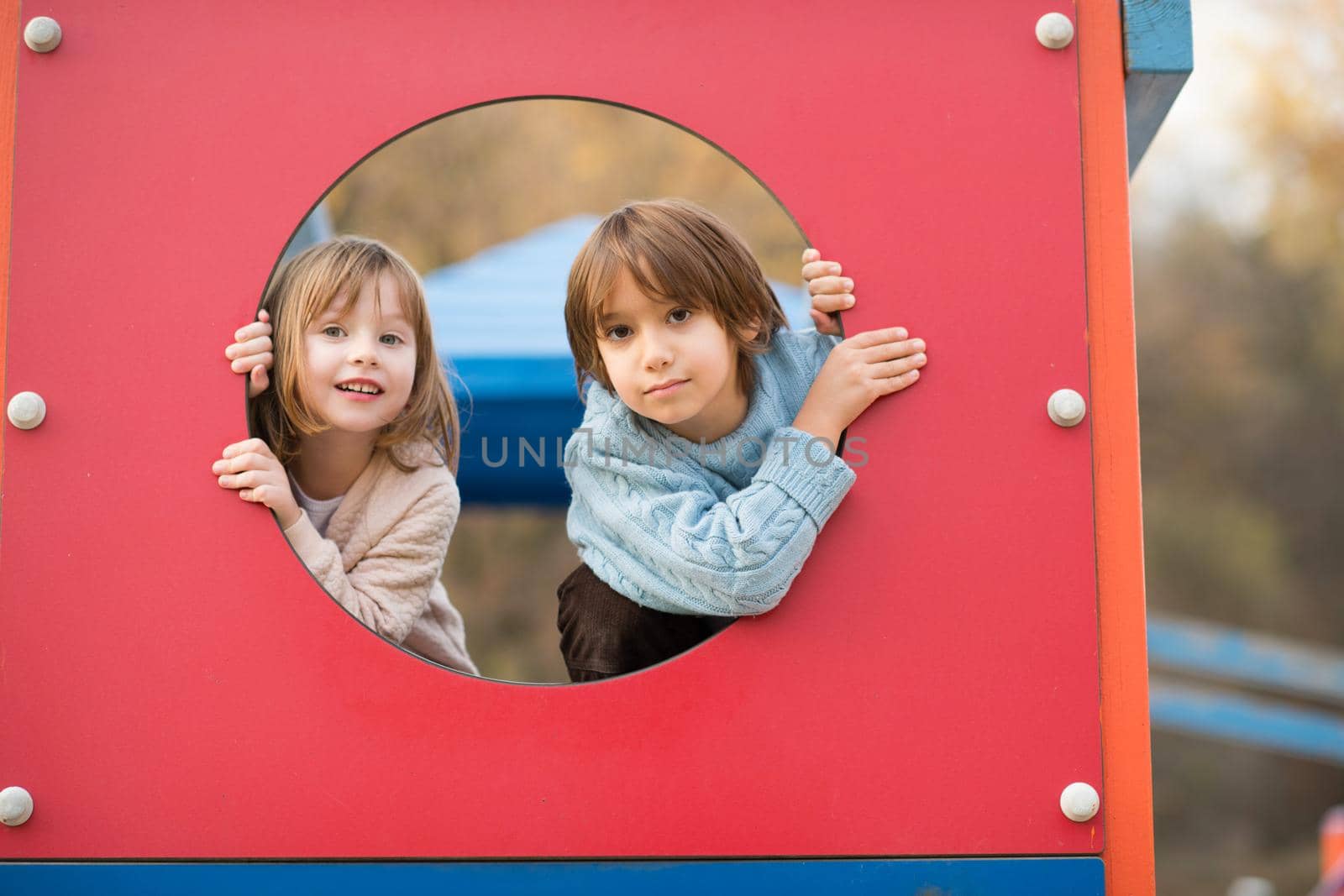 cutte little girl and boy in childrens park having fun and joy while playing in playground on autumn cloudy day