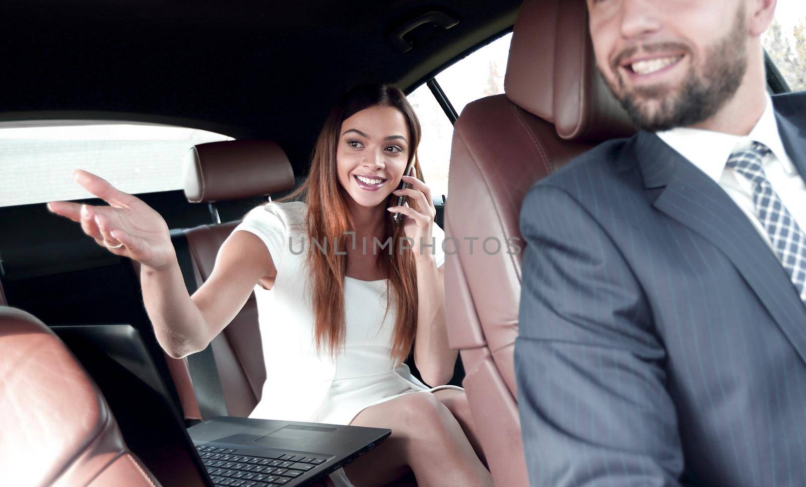 Businesswoman on the backseat with elegant man driving a car in the city.