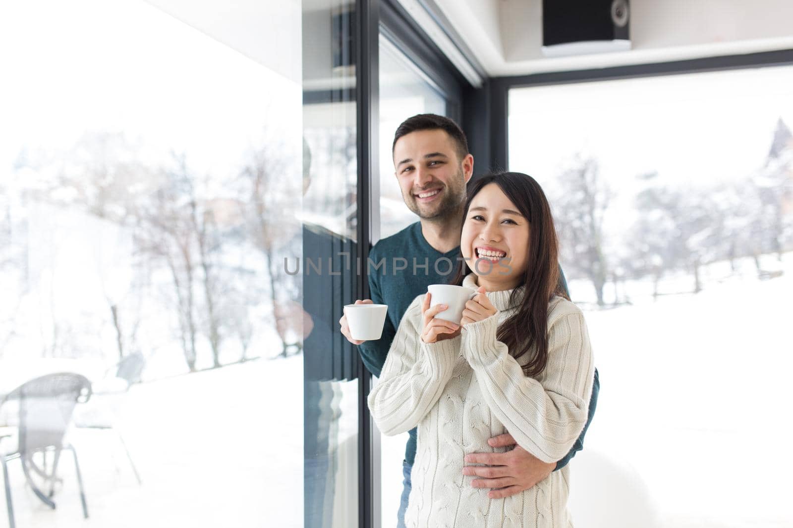 happy young multiethnic couple enjoying morning coffee by the window on cold winter day at home