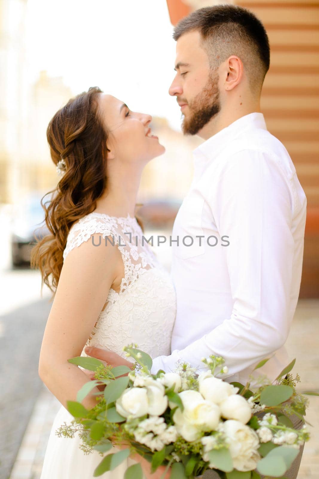 Happy groom hugging fiancee keeping flowers and wearing white dress. by sisterspro