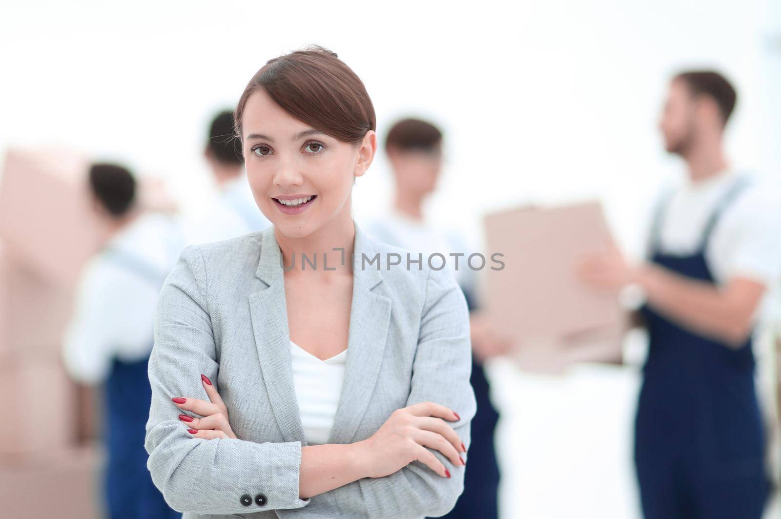 Smiling manager holding clipboard on blurred background with movers and boxes.