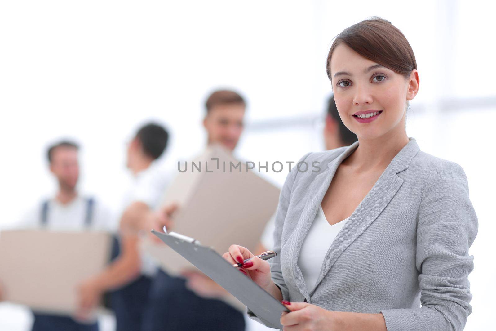 Woman manager holding clipboard on blurred background with movers and boxes.