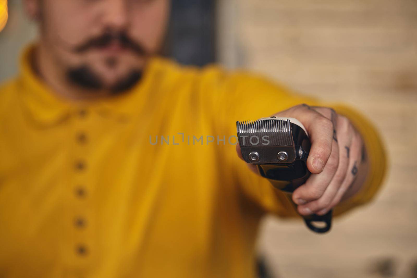 Stylish barber man with mustache in yellow t-shirt showing his hairdressing tools before work